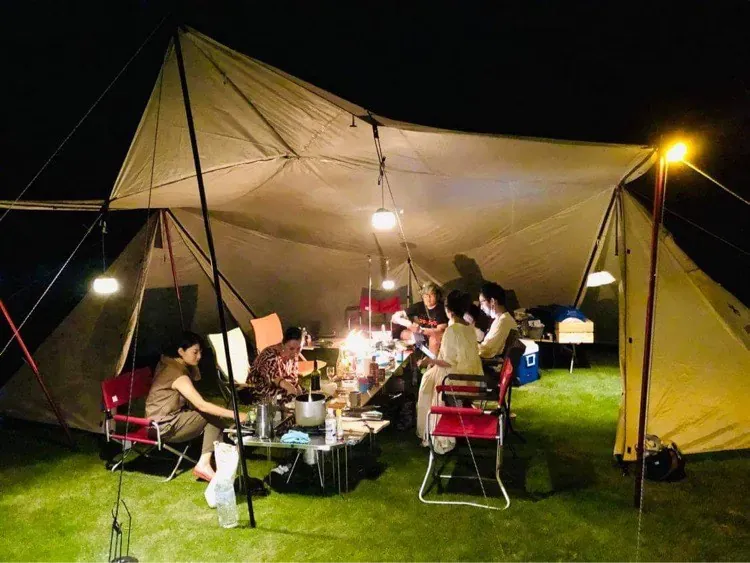 夜、芝生の庭に張ったタープの下でテーブルを囲む滞在者たち