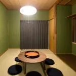 緑色の壁の部屋に置かれた円形のちゃぶ台と座布団